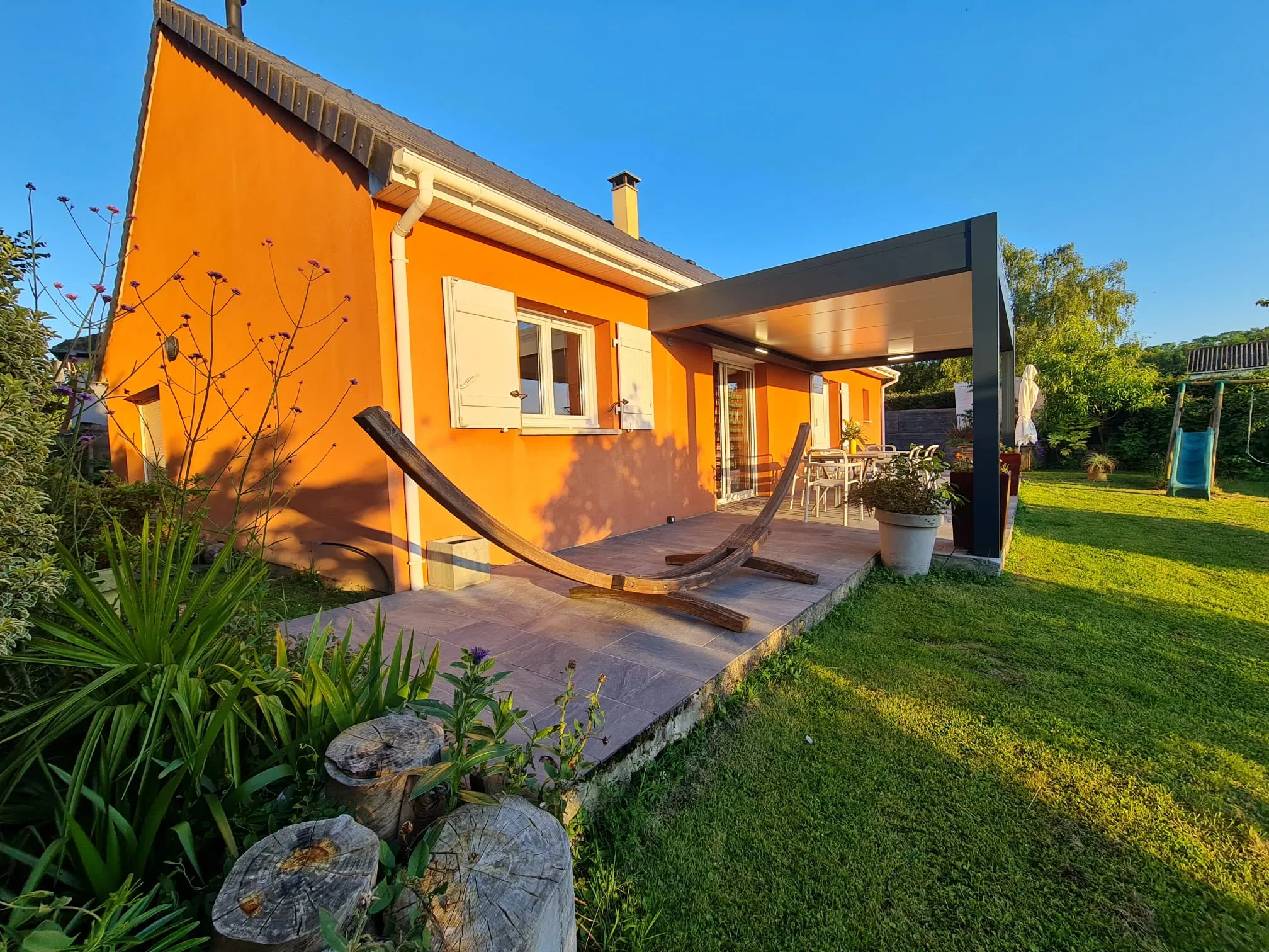La maison de plain-pied et sa terrasse couverte au soleil couchant