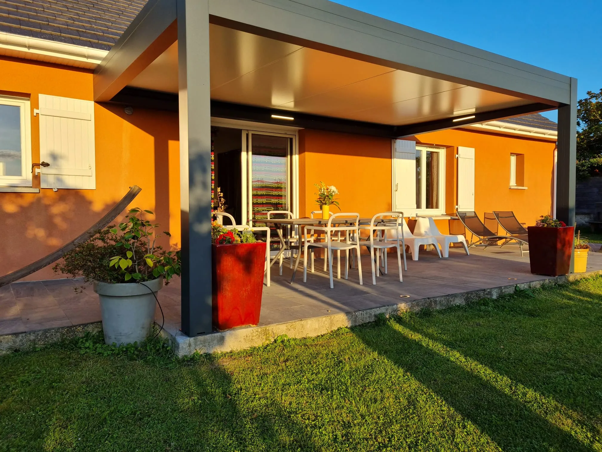 La terrasse couverte avec table, chaises et baies vitrées du séjour